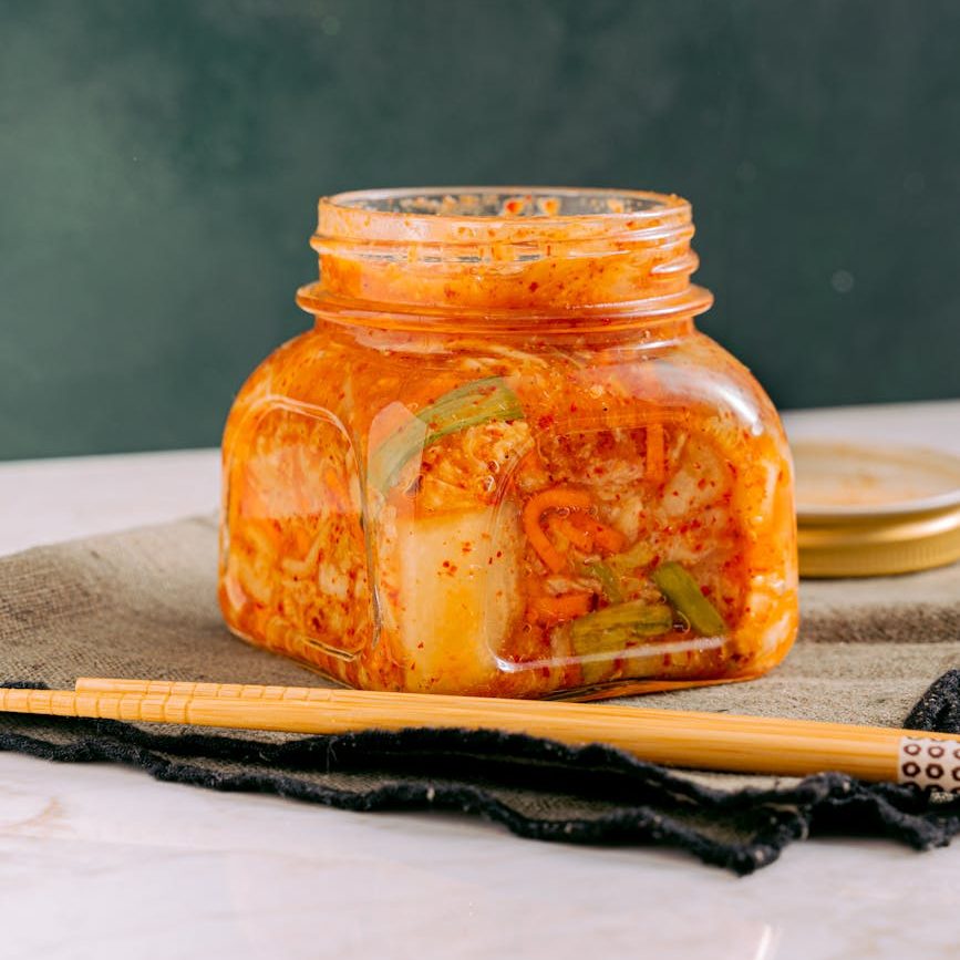 clear glass jar with kimchi beside the wooden chopsticks