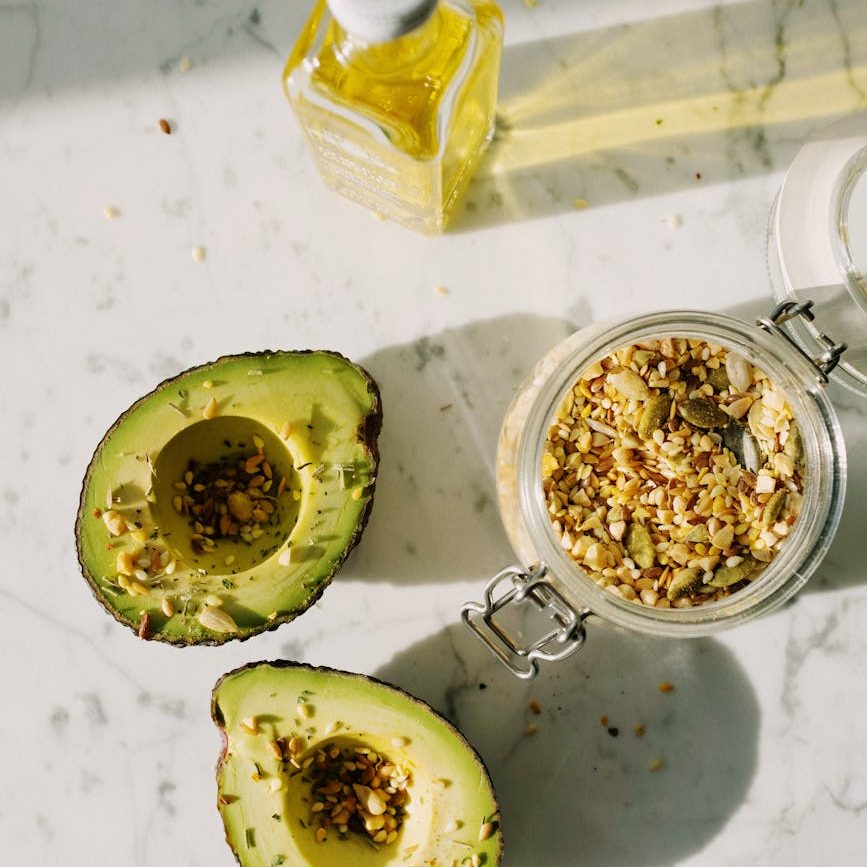 delicious halved avocado with various seed grains and olive oil on marble surface