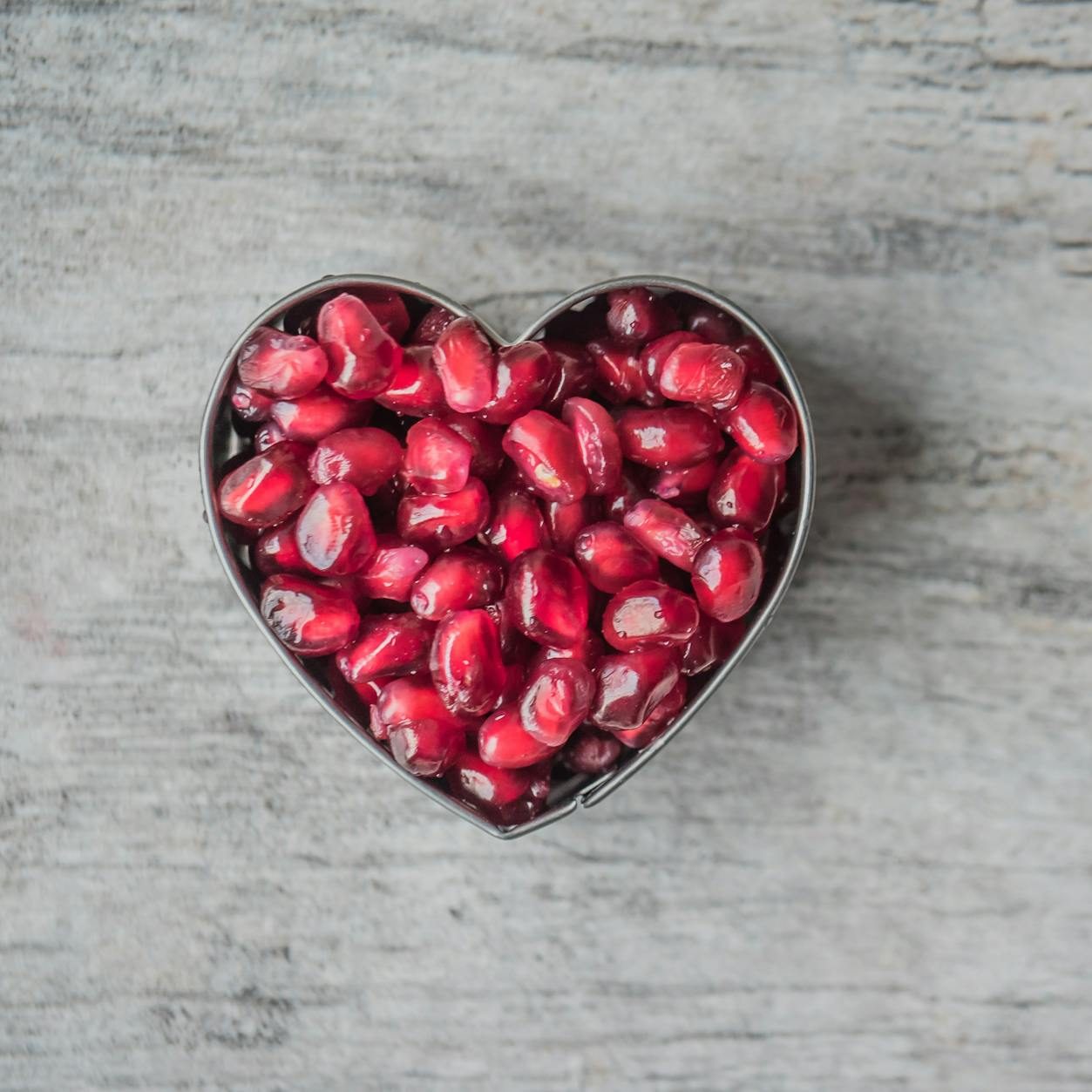 silver heart bowl filled of red pomegranate seeds