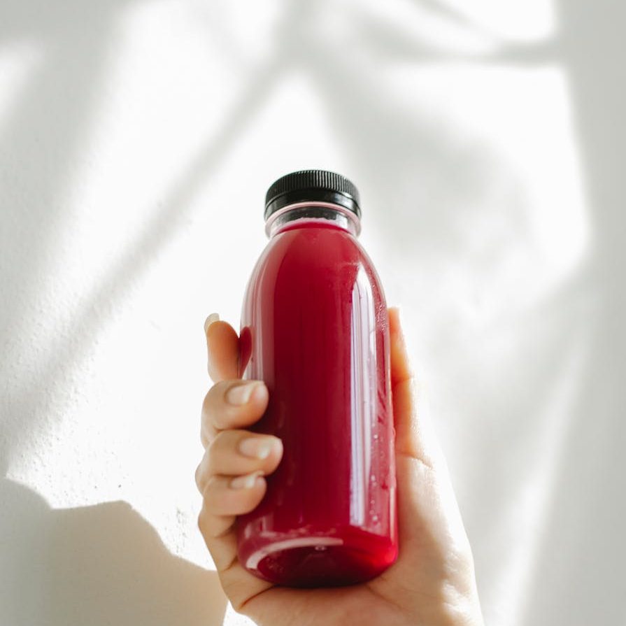 unrecognizable woman holding bottle of red juice against white wall