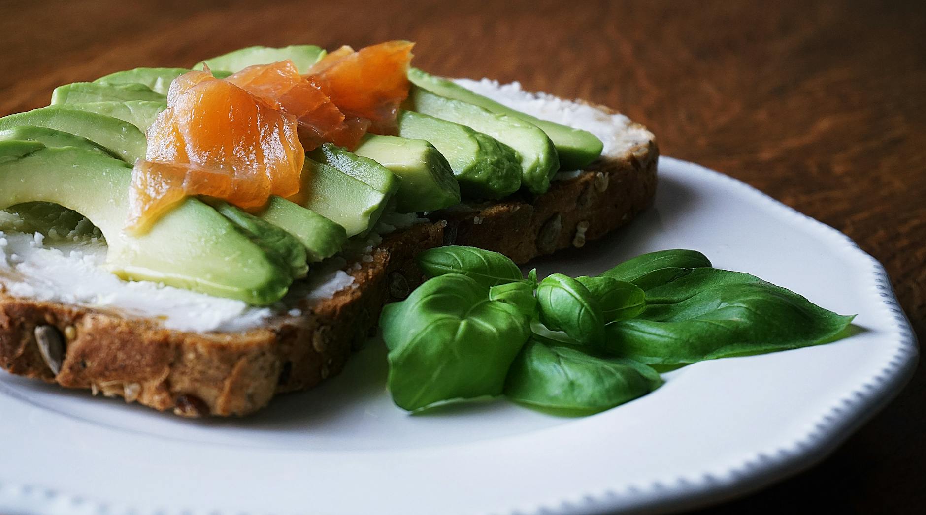 bread with sliced avocado and salmon near basil mint on plate