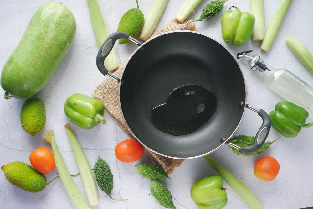 cooking pot with oil surrounded by fresh vegetables