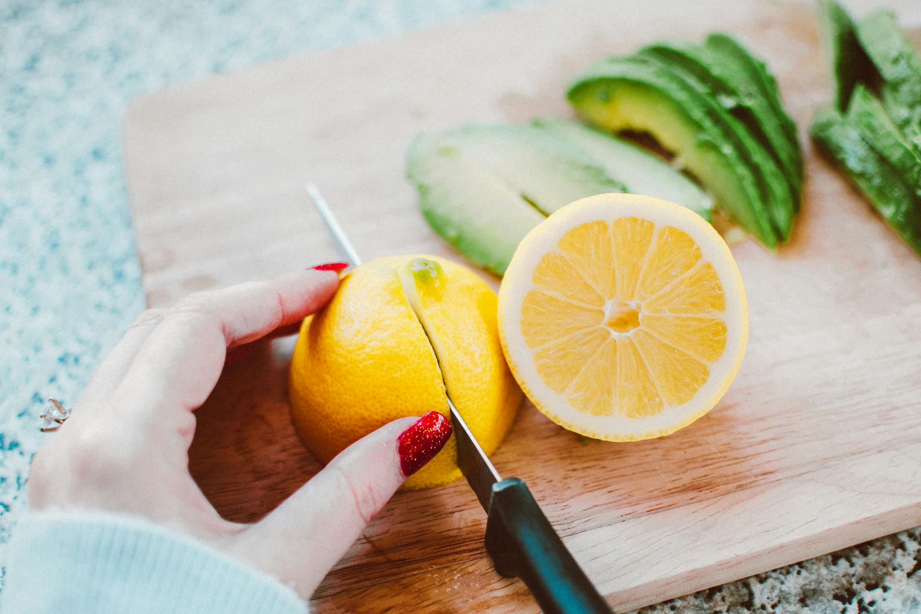 person slicing lemon on wooden chopping board