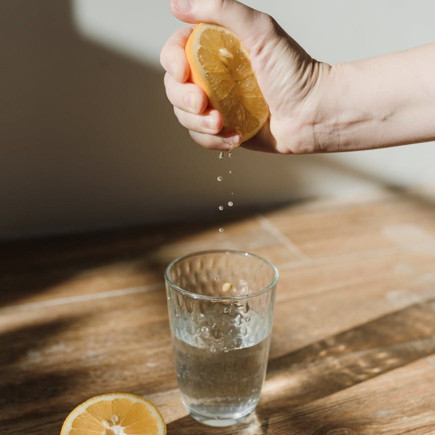 a person squeezing a lemon in a glass of water