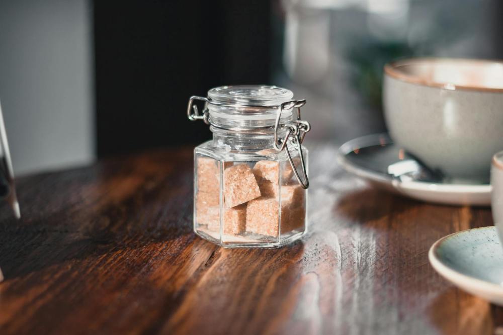 clear condiment shaker with brown sugar cubes near gray teacup