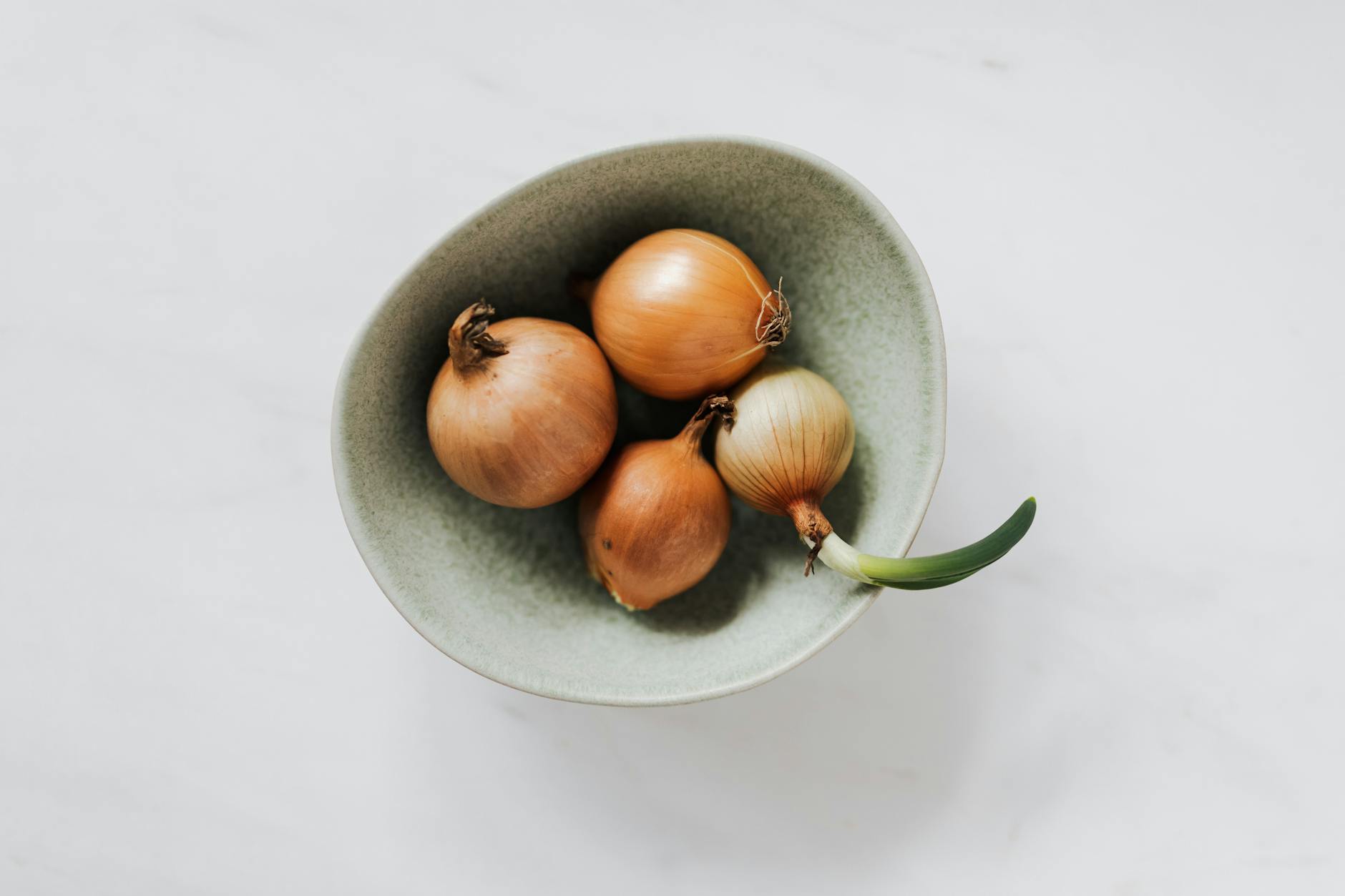 bowl with raw onion bulbs on marble surface